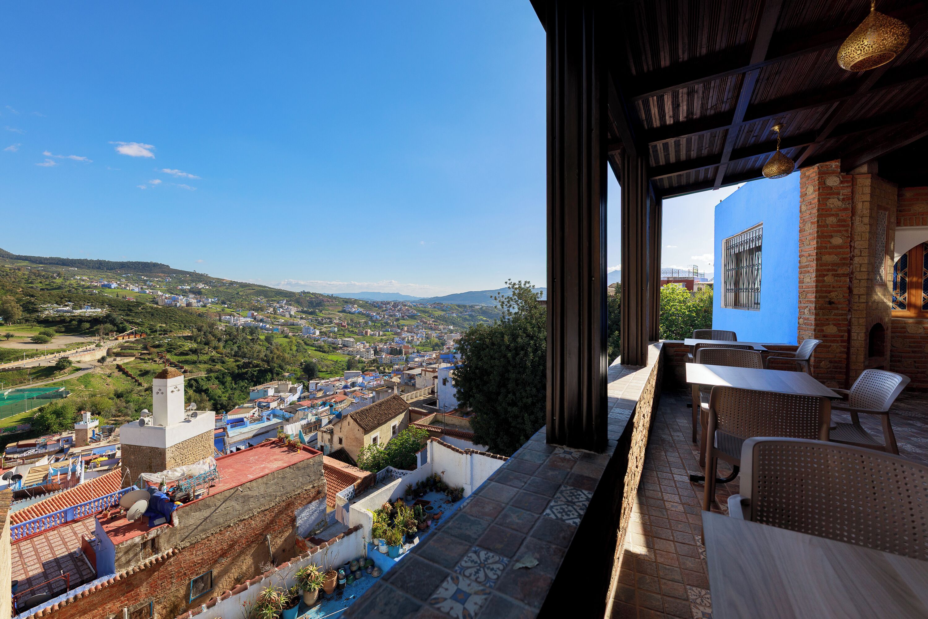 A terrace with a view of a town, outdoor seating, and a building with a blue facade.