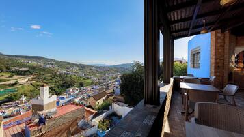 A terrace with a view of a town, outdoor seating, and a building with a blue facade.
