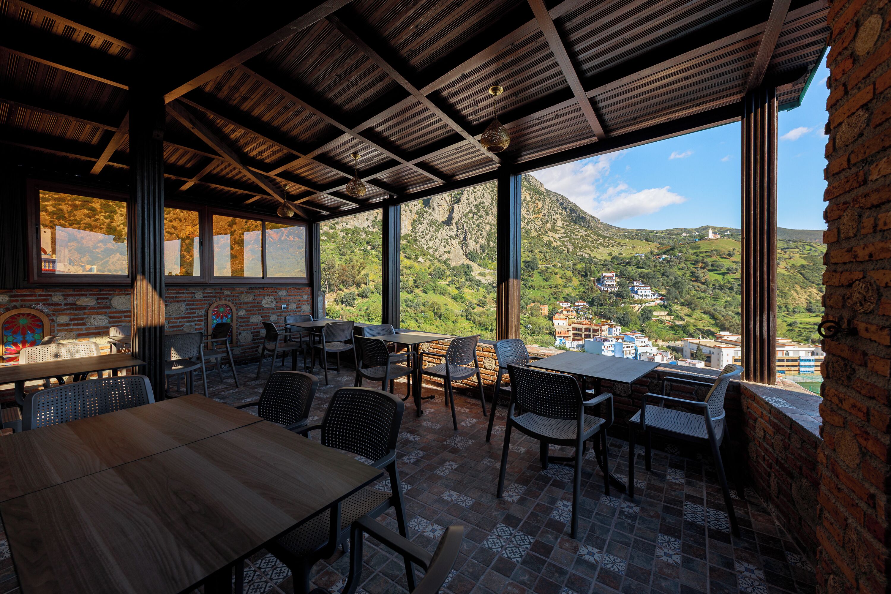An outdoor dining area with tables and chairs, a brick wall, and a view of a mountainous landscape.