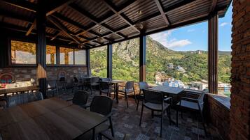 An outdoor dining area with tables and chairs, a brick wall, and a view of a mountainous landscape.