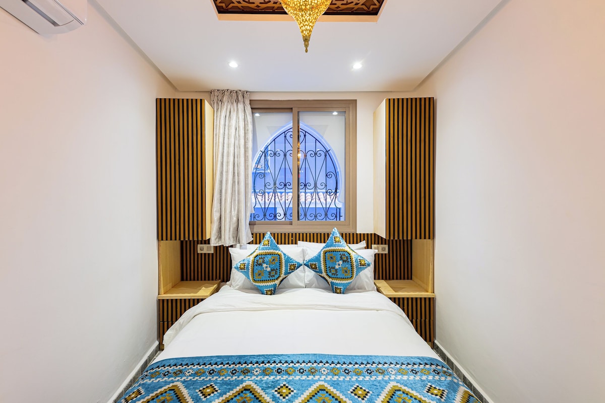 A bedroom with a bed, a window with a decorative metal gate, and a chandelier.