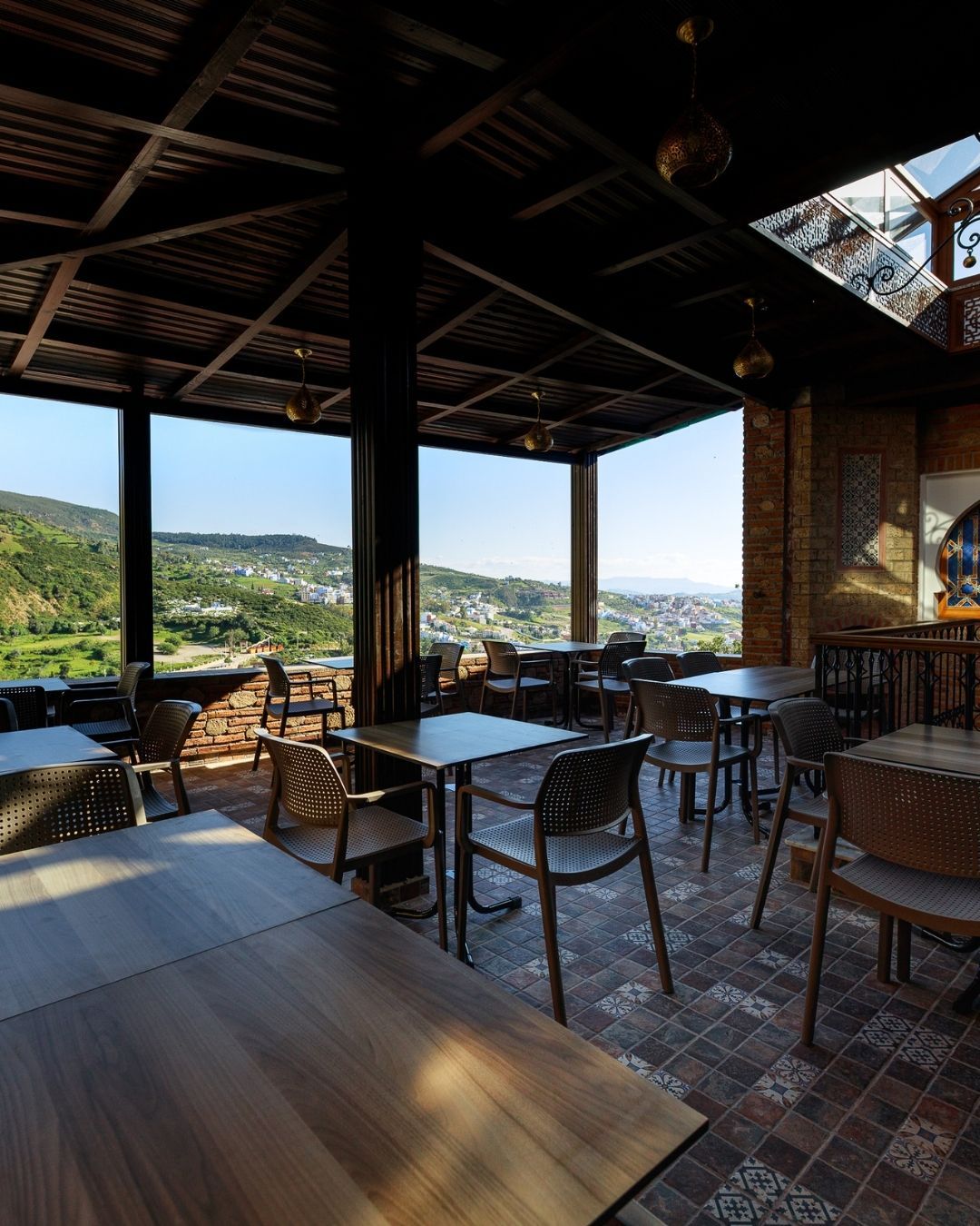 Un espacio de comedor al aire libre con mesas y sillas, ventanas amplias y vistas al campo.