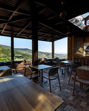 An outdoor dining area with tables and chairs, large windows, and a view of the countryside.