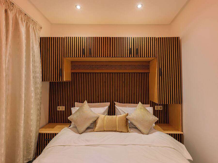 Een slaapkamer met een bed, kussens, een houten hoofdbord, nachtkastjes en een gordijn.