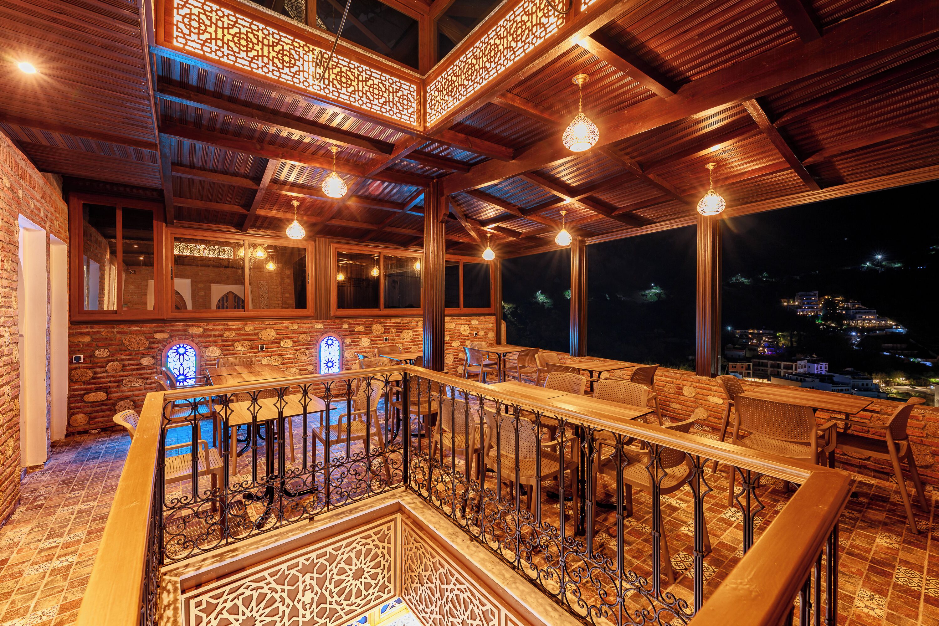 An interior with wooden beams, a balcony with seating, and a view of the city at night.