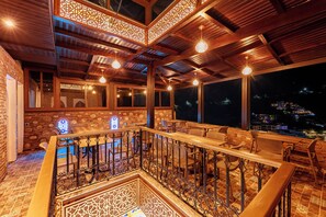 An interior with wooden beams, a balcony with seating, and a view of the city at night.
