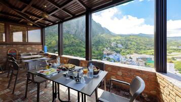 A dining area with a table set for two, overlooking a mountainous landscape.