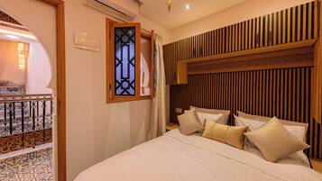 A hotel room with a bed, a decorative wall panel, a window with a view, and an air conditioning unit.