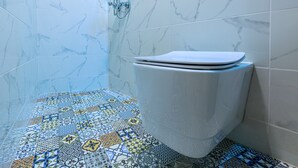 A bathroom with a toilet, a shower, and a tiled floor with a geometric pattern.
