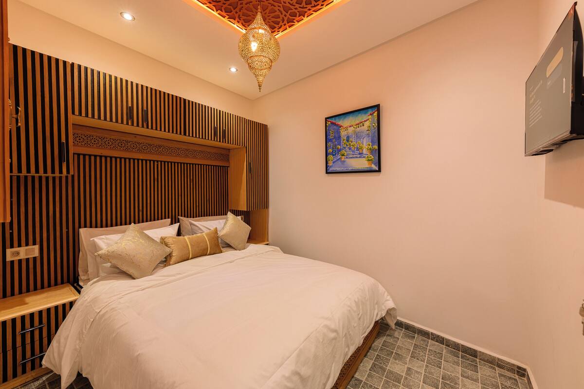 A hotel room with a bed, wooden paneling, a television, and a painting on the wall.