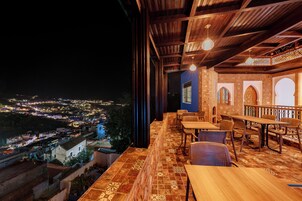 Una terraza con vistas a una ciudad de noche, que incluye una mesa, sillas, un suelo con diseño y un techo de madera.