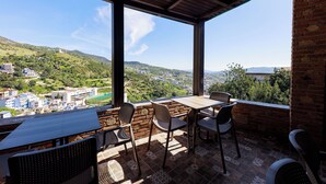 Eine Terrasse mit Tisch und Stühlen, mit Blick auf ein Tal mit Gebäuden und viel Grün.