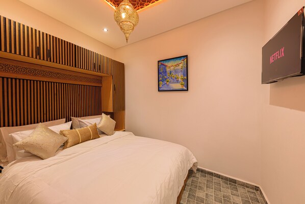 A hotel room with a bed, wooden panel wall, decorative ceiling light, artwork, and a television mounted on the wall. - Riad Seddiki (Chefchaouen)