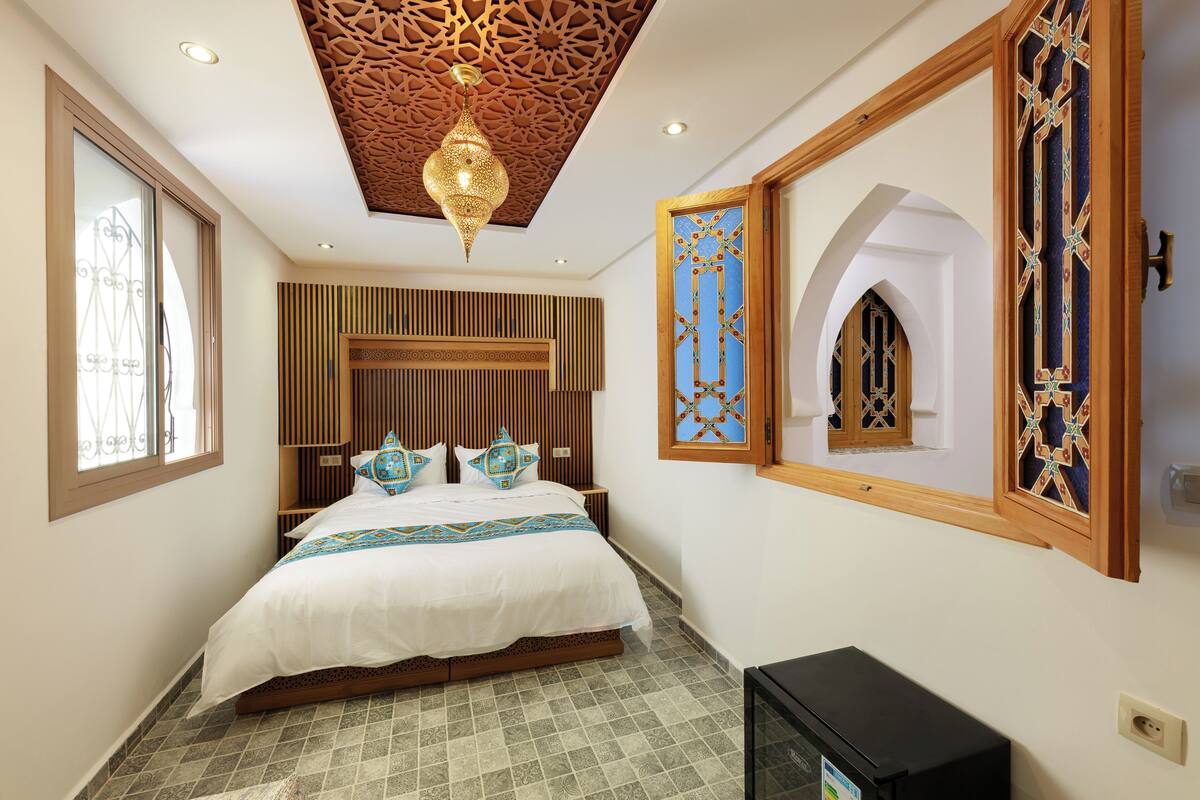 A bedroom with a bed, a TV, a decorative ceiling, and a window.