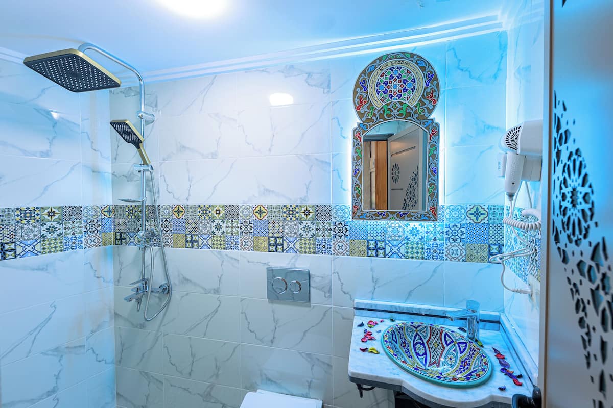 A bathroom with a shower, a sink with a decorative basin, a mirror with an ornate frame, and a wall with patterned tiles.