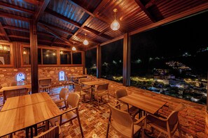 An outdoor dining area with wooden tables and chairs, a brick wall, and a view of a cityscape at night. - Riad Seddiki (Chefchaouen)