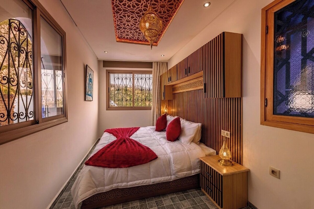 Une chambre à coucher avec un lit, une table de chevet, un plafond décoratif et une fenêtre donnant sur un beau paysage.