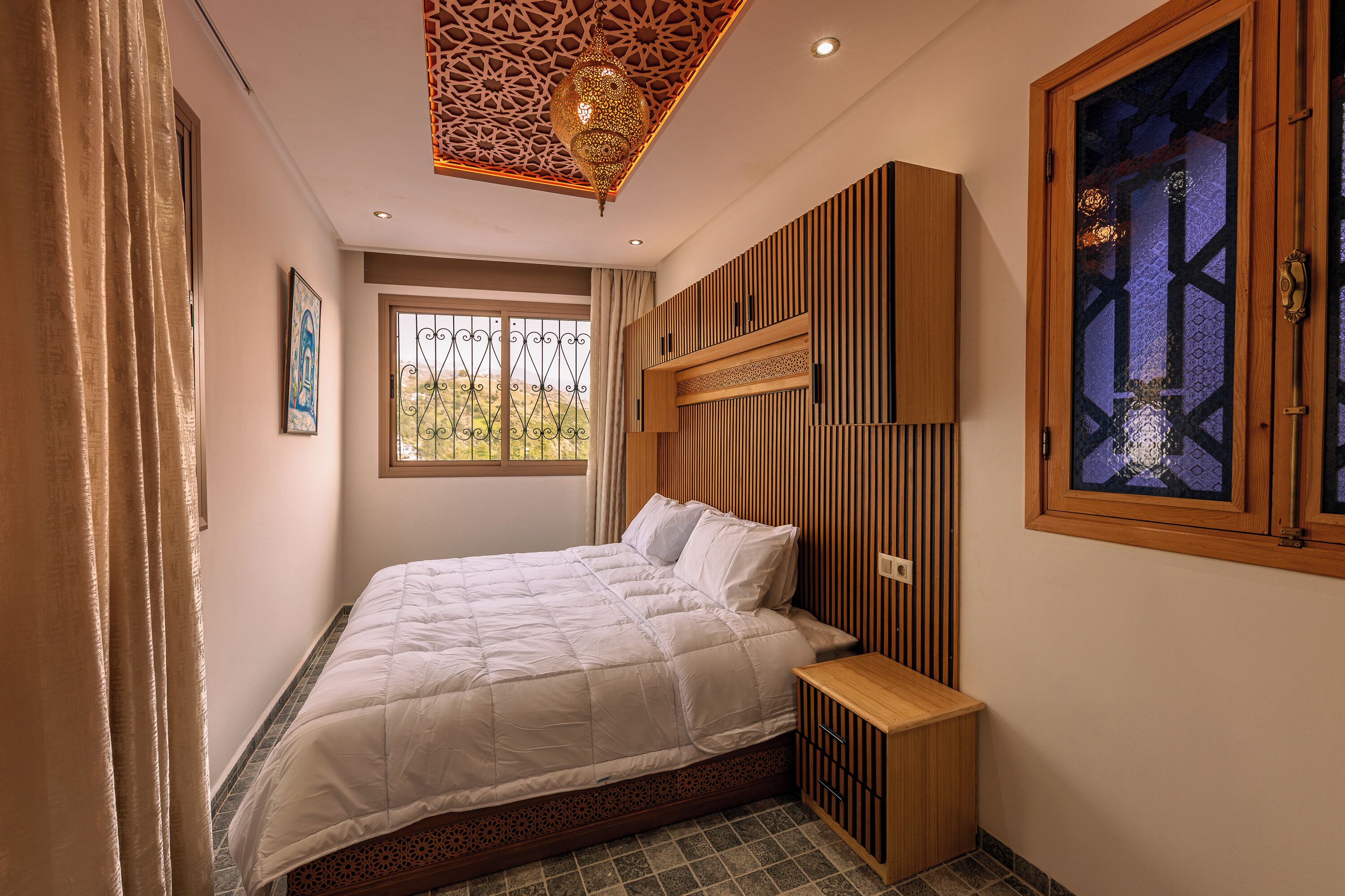 Un dormitorio con cama, mesita de noche, techo decorativo, ventana con vistas y un armario de pared.