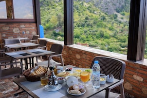 Una mesa de desayuno con diversos alimentos y una botella de agua, con un fondo de pared de ladrillo y una vista panorámica.