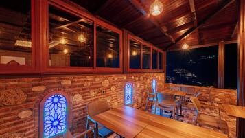 Un restaurante con mesas y sillas de madera, ventanas amplias y vistas a la ciudad de noche.