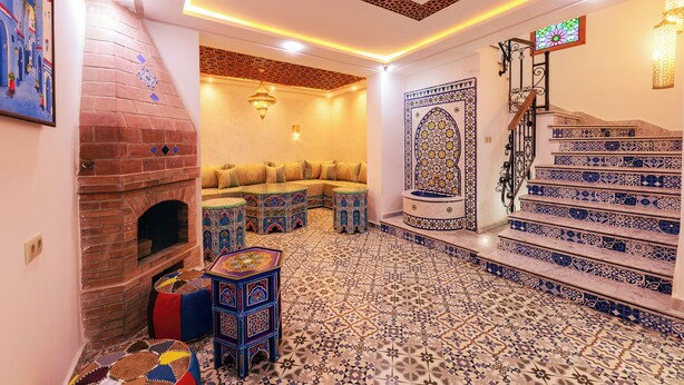 A room with a brick fireplace, a sofa, patterned tiles, and a staircase with blue and white tiles.