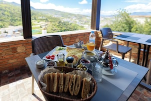 Una mesa dispuesta con diversos alimentos, incluyendo pan, aceitunas y una bebida, con una vista panorámica al fondo.