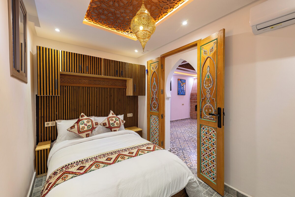 Un dormitorio con una cama, una mesita de noche, una lámpara decorativa en el techo y una puerta con diseños intrincados.