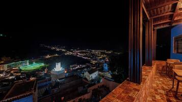 A night view from a balcony with a cityscape in the background, a terrace with a patterned floor, and a view of a lit-up sports field.