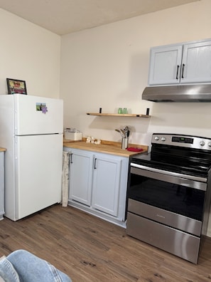 A compact kitchen with a refrigerator, oven, and a wooden countertop.