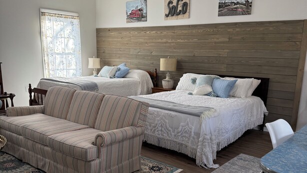 Quarto com duas camas, um sofá, uma mesa de jantar e um tapete estampado.