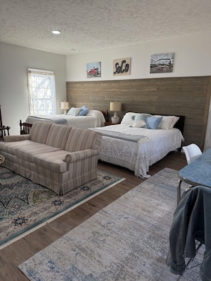 A bedroom with two beds, a sofa, a dining table, and a patterned rug.