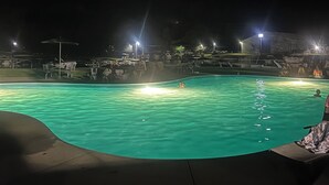 Una piscina notturna con acqua cristallina, circondata da un’area scura con luci in lontananza.