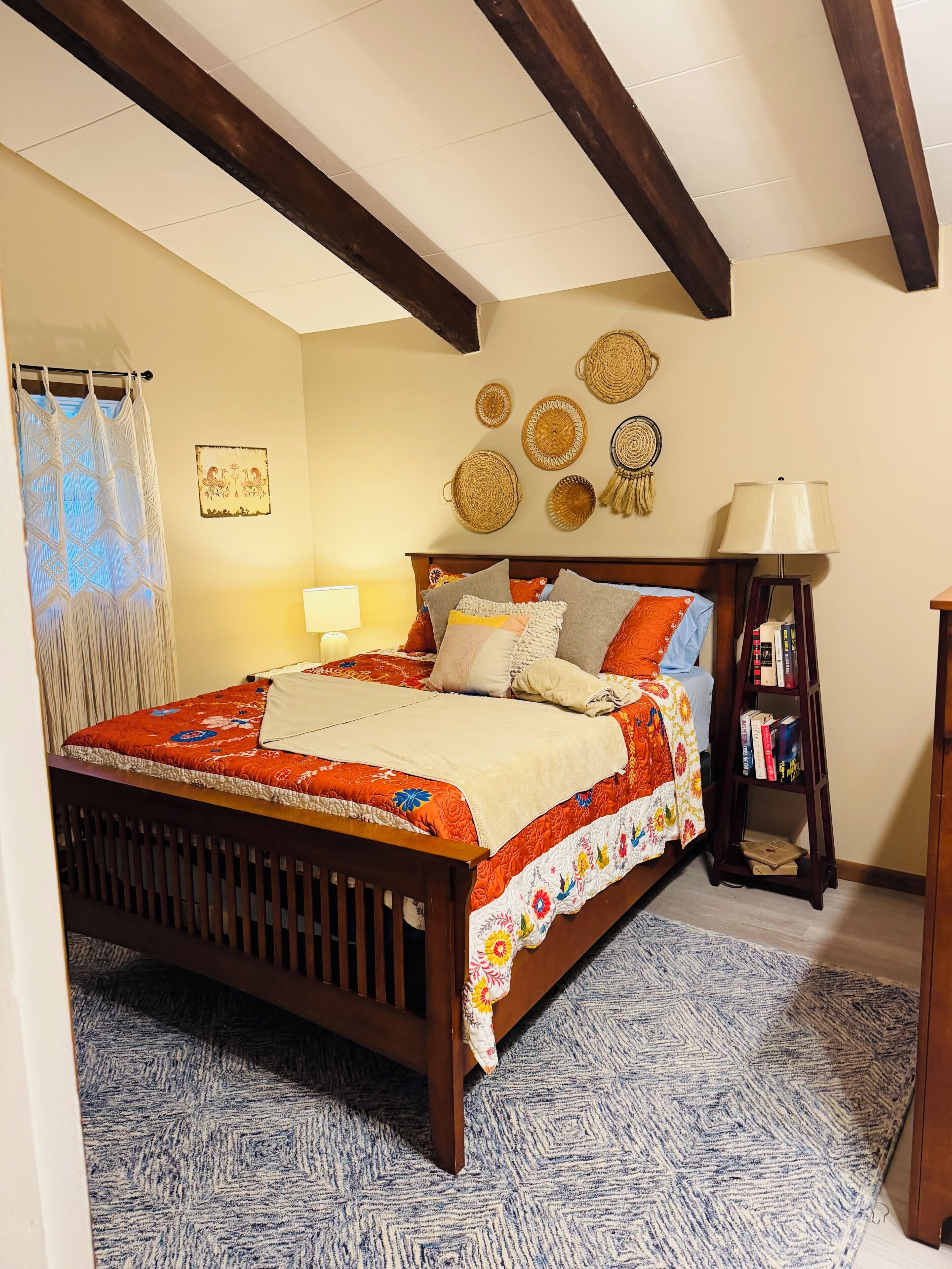 A bedroom with a wooden bed, a bedside lamp, a wall with woven baskets, and a patterned rug.