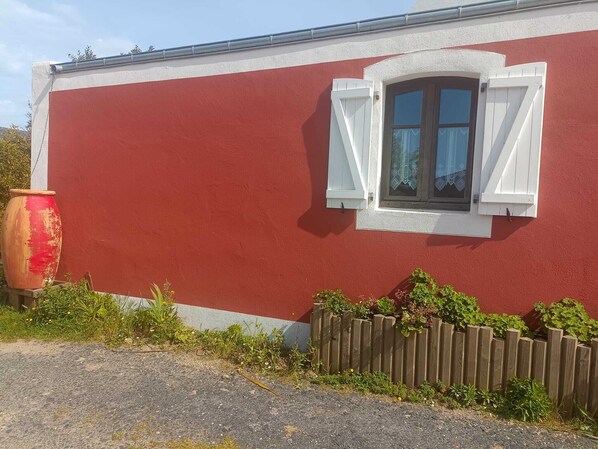 A red building with a white window and shutters, a wooden fence, and a large red pot. - Studio Kokon Holz & Design - near GR, Le Palais, and the beach (Le Palais)