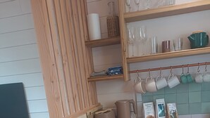 A kitchen with wooden cabinets, a white refrigerator, and shelves with glassware and kitchen items. - Studio cocoon wood & design - near GR + Le Palais + Plage (Le Palais)