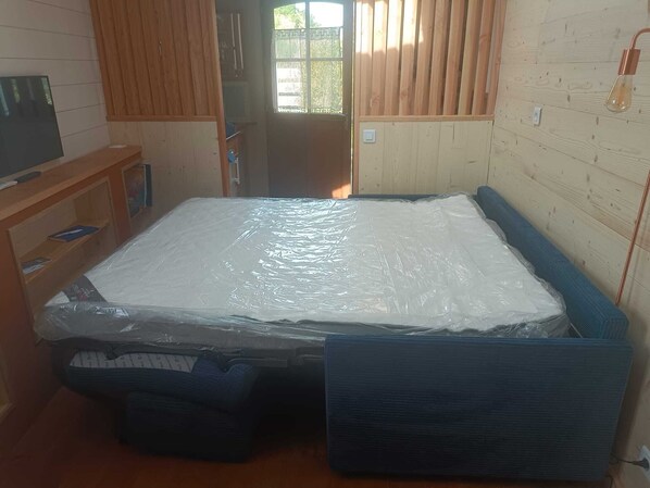 Una habitación con una cama cubierta de plástico, paredes de madera, una ventana y una puerta.