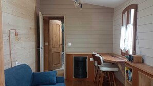 A compact living space with a sofa, a small kitchen area, and a ceiling fan. - Studio cocoon wood & design - near GR + Le Palais + Plage (Le Palais)