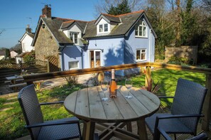 A house with a blue exterior, a wooden deck, and a round wooden table with chairs. - Ty Mari Crydd, Eglwyswrw (Eglwyswrw)