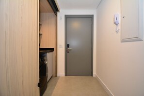 Un pasillo estrecho con una puerta cerrada, una lavadora y un teléfono en la pared.