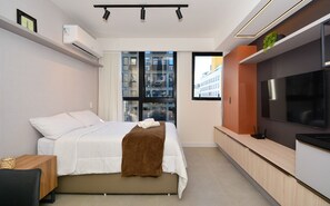 Un dormitorio moderno con cama, televisión y ventana con vista a la ciudad.