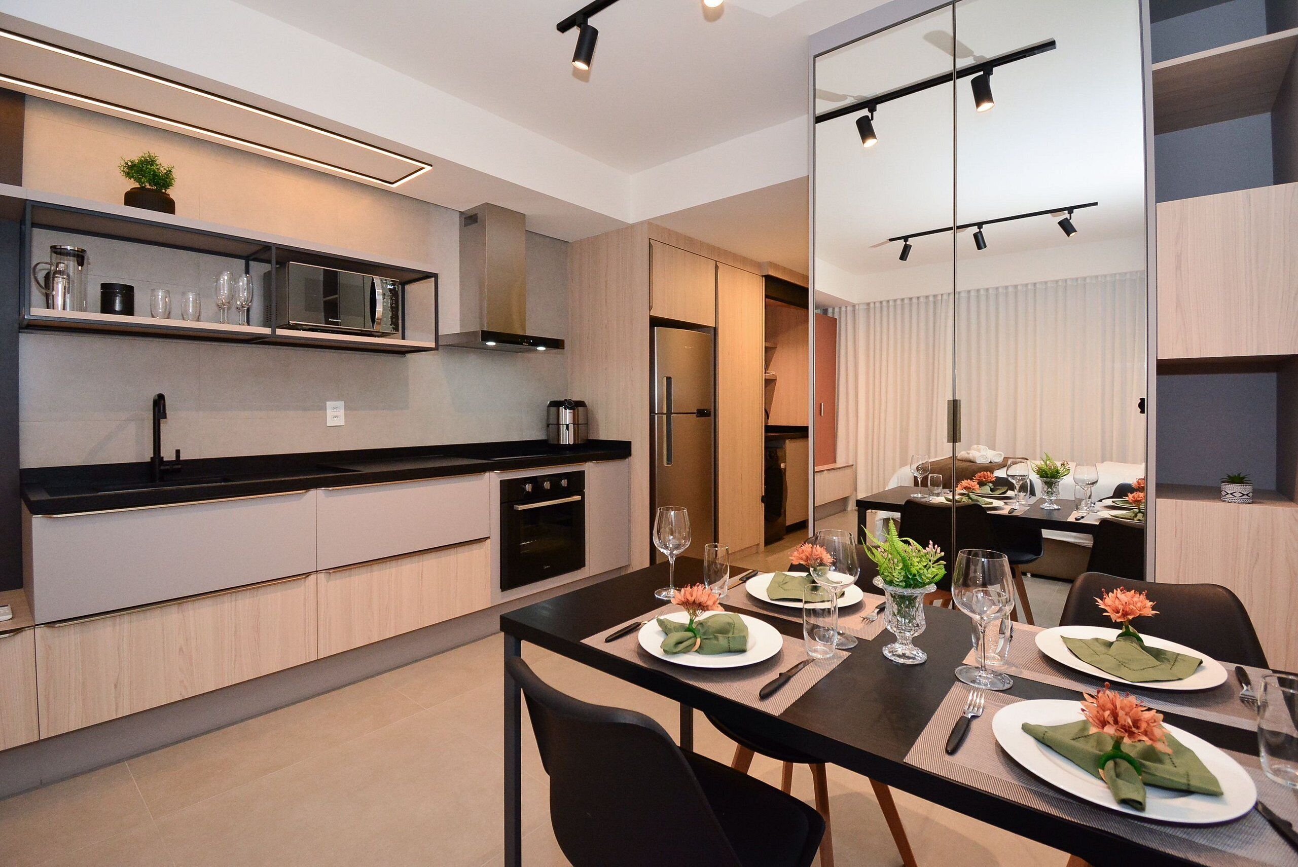A modern kitchen with a dining area, featuring a black countertop, stainless steel appliances, and a dining table set with plates and glasses.