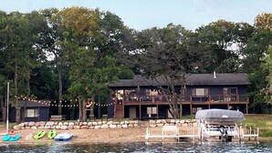 A lakeside cabin with a dock, kayaks, and a covered boat.