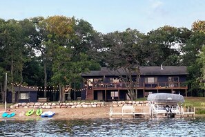 A lakeside cabin with a dock, kayaks, and a covered boat.