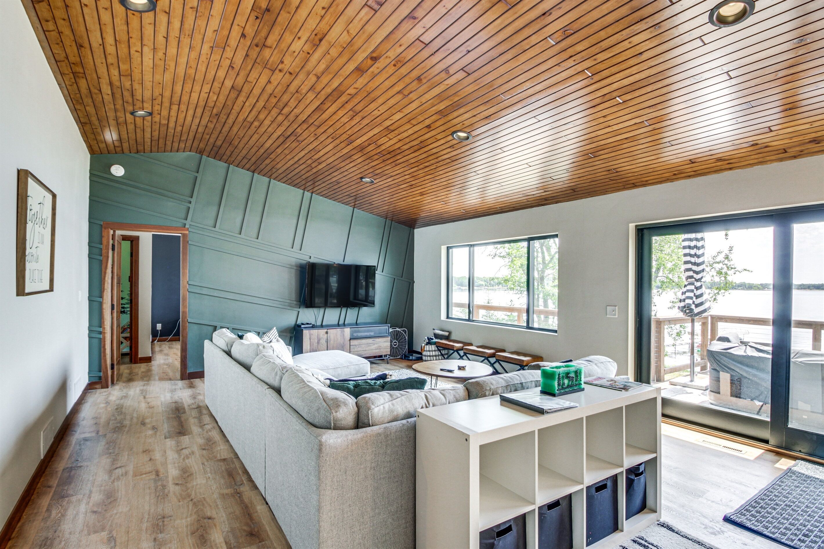 Una sala moderna con techo de madera, un ventanal grande, un sofá, un televisor y un comedor.