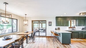 A modern kitchen with green cabinets, a large island, and a dining area with wooden tables and chairs.