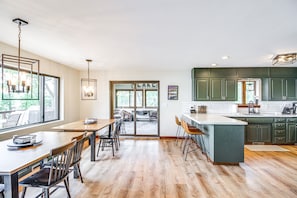 A modern kitchen with green cabinets, a large island, and a dining area with wooden tables and chairs.