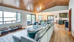 A spacious living area with a wooden ceiling, large windows, a kitchen, and a dining area.