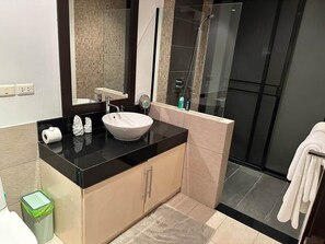 Een moderne badkamer met een zwart aanrecht, een wit wastafel, een spiegel en een douchegedeelte.