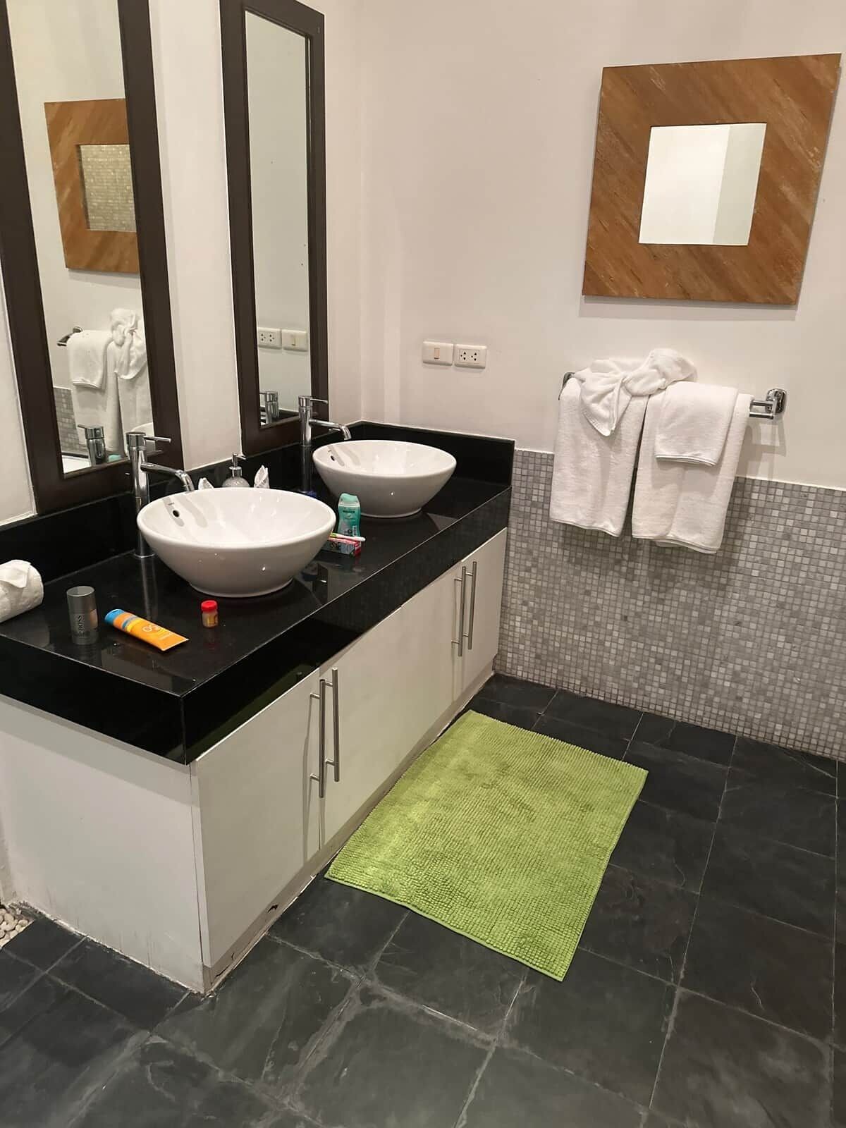 A bathroom with two sinks, a large mirror, a towel rack, and a green rug.