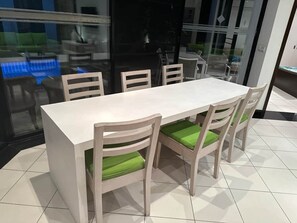 Een eetgedeelte met een witte tafel en vier stoelen met groene kussens.